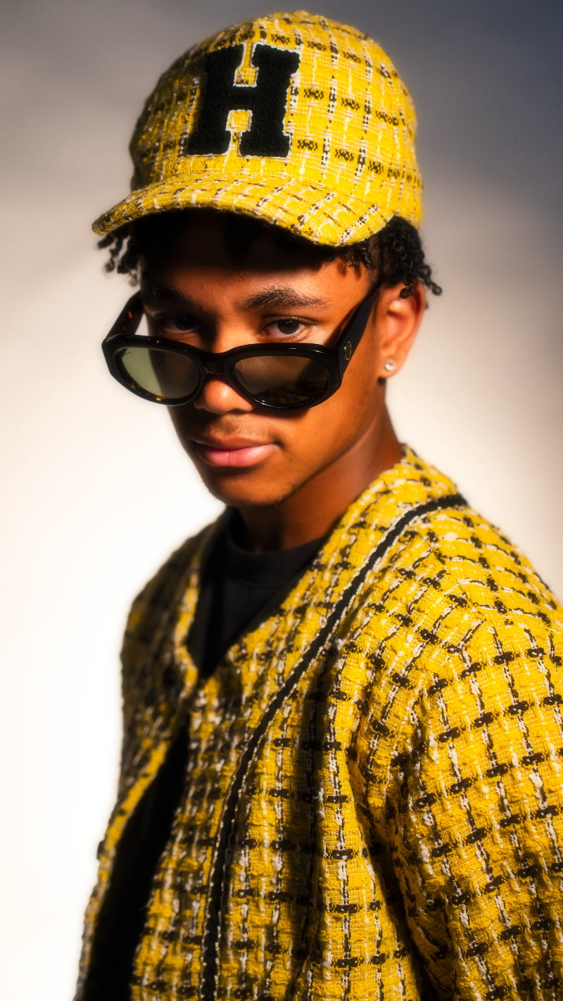 Person wearing a yellow cap with a black 'H' logo and sunglasses, against a neutral background
